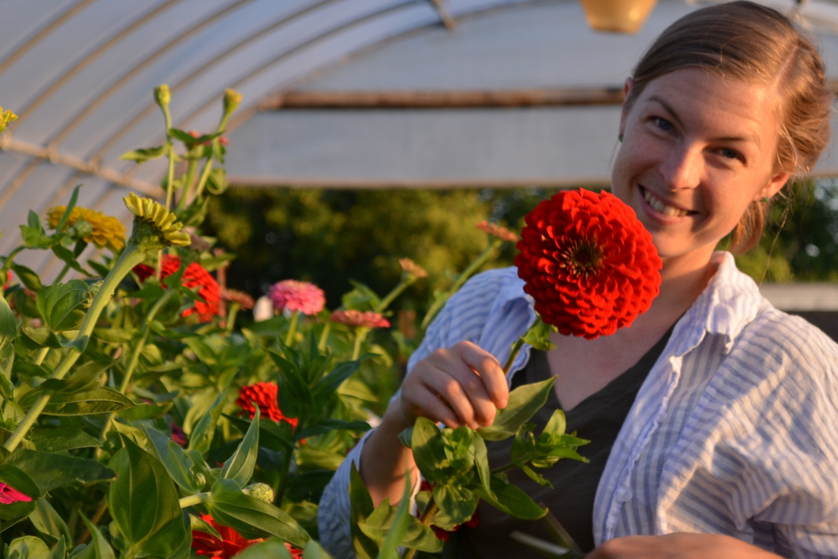 anna merkt smiles in a headshot with cherry red zinnia flower as big as her face